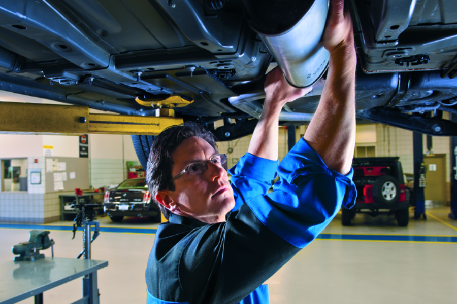 A man in a blue shirt repairs a vehicle, focused on the engine with tools scattered around him in a garage setting.